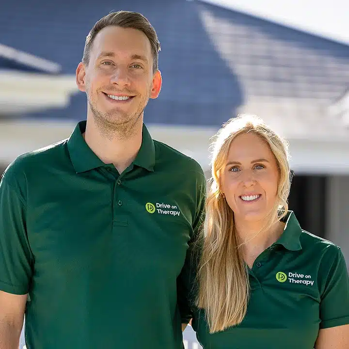 Two Drive on Therapy team members smiling and standing outdoors in uniform polo shirts.
