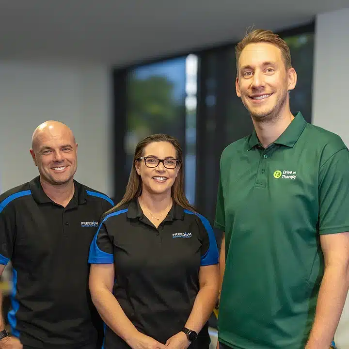 Team members from Drive on Therapy and Freedom Motors standing together indoors, smiling at the camera.