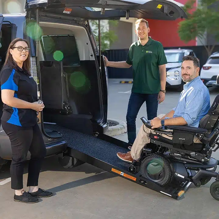 Occupational therapist standing with a client in a wheelchair at the rear of a modified van with a ramp.