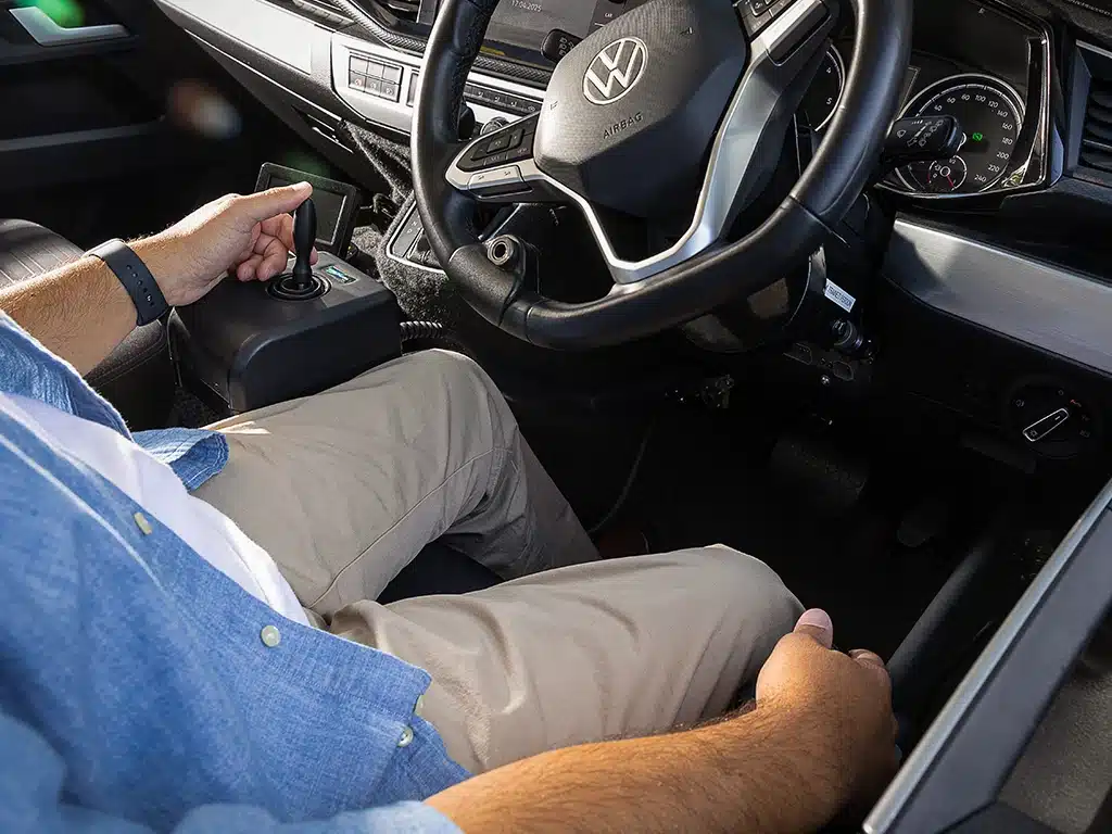 Interior view showing a person using joystick controls in a Volkswagen vehicle during a driving session.