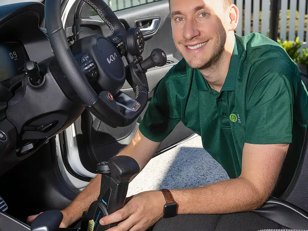 Driving rehabilitation specialist adjusting hand controls in an adapted vehicle for driver assessment and training.