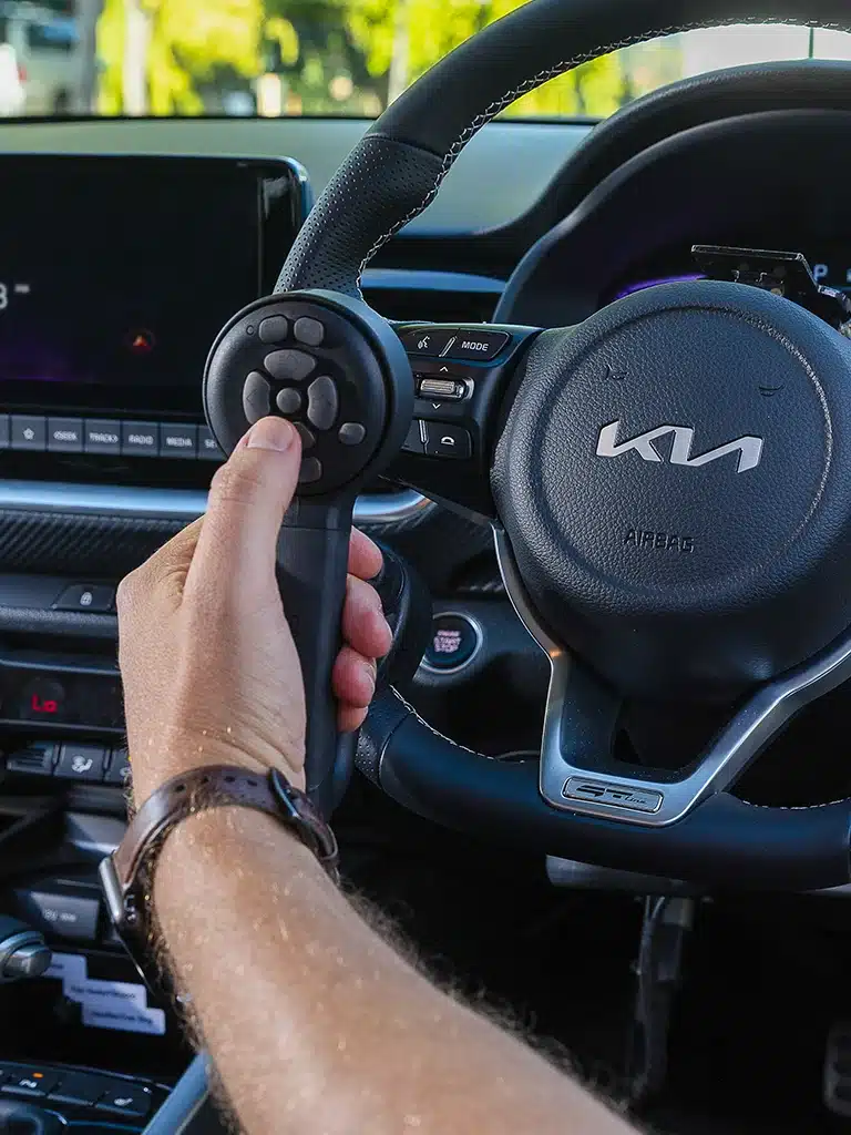 Driver holding a multi-function joystick for adaptive vehicle control, inside a modified car.
