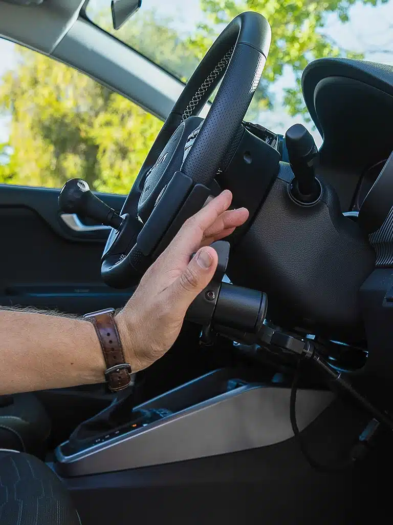 Side view of hand activating electronic hand control system in a vehicle with adaptive driving equipment.
