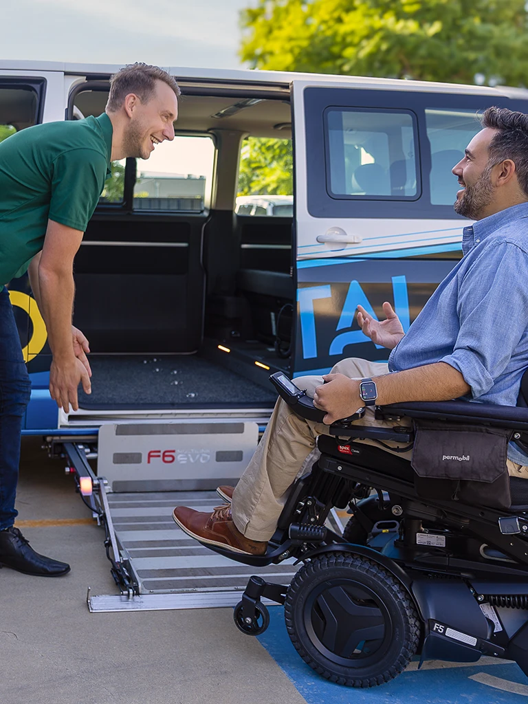 Man in a Permobil power wheelchair preparing to board an accessible vehicle via rear entry ramp.