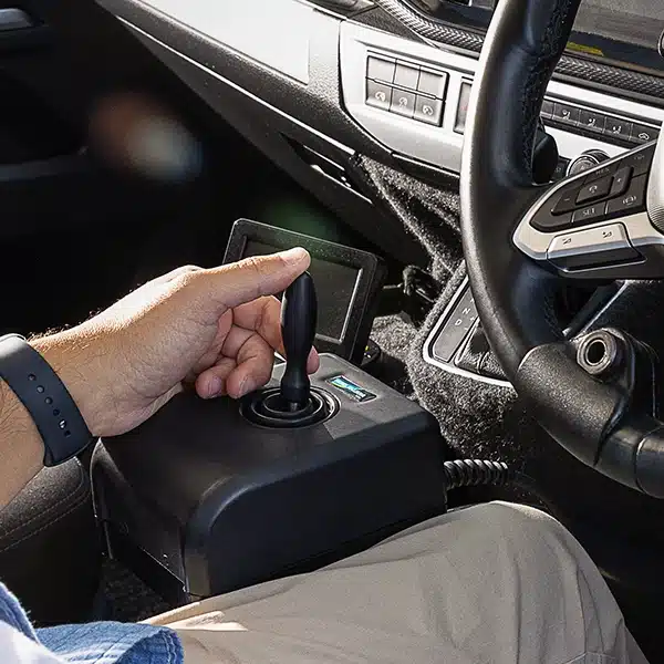 Driver using a 4-way joystick control system integrated into an accessible vehicle, with the control mounted between the seats.